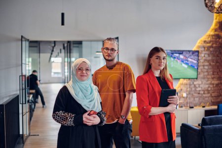 Photo for A group of young business colleagues, including a woman in a hijab, stands united in the modern corridor of a spacious startup coworking center, representing diversity and collaborative spirit - Royalty Free Image