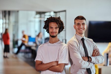 Eine Gruppe von Kollegen, darunter ein afroamerikanischer Geschäftsmann und ein junger Führer in Hemd und Krawatte, posieren gemeinsam in einem modernen Coworking Center-Büro und repräsentieren eine dynamische Mischung aus