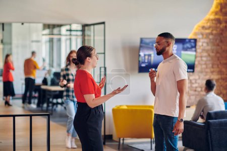 Photo for Young business colleagues, including an African American businessman, engage in a conversation about business issues in the hallway of a modern startup coworking center, exemplifying dynamic problem - Royalty Free Image
