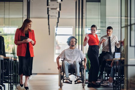 Photo for A group of young business people in a modern glass-walled office captures the essence of diversity and collaboration, while two colleagues, including an African American businessman in a wheelchair - Royalty Free Image