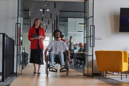 Téléchargez les photos : Un groupe de jeunes gens d'affaires dans un bureau moderne aux murs de verre saisit l'essence de la diversité et de la collaboration, tandis que deux collègues, dont un homme d'affaires afro-américain en fauteuil roulant - en image libre de droit
