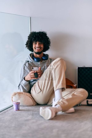 Photo for African-American entrepreneur taking a relaxing break from work, sitting on the floor while using wireless headphones and a smartphone for some digital entertainment - Royalty Free Image