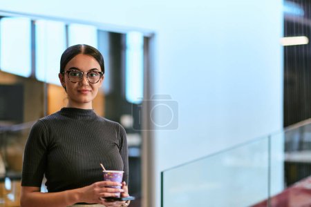 Photo for In a bustling modern office a businesswoman in glasses juggles her tasks, sipping coffee and using her smartphone, epitomizing the dynamic and multitasking nature of contemporary corporate life. - Royalty Free Image