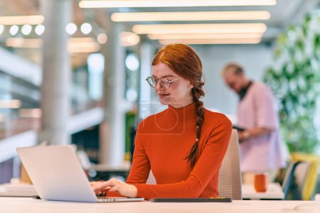 Photo for In a modern startup office, a professional businesswoman with orange hair sitting at her laptop, epitomizing innovation and productivity in her contemporary workspace - Royalty Free Image