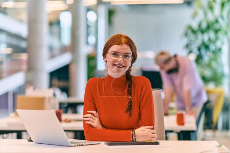 Photo for In a modern startup office, a professional businesswoman with orange hair sitting at her laptop, epitomizing innovation and productivity in her contemporary workspace - Royalty Free Image