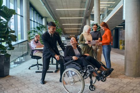 A diverse group of business colleagues is having fun with their wheelchair-using colleague, demonstrating their attention and inclusivity in the workplace. 