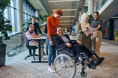 Téléchargez les photos : Un groupe diversifié de collègues d'affaires s'amuse avec leur collègue qui utilise un fauteuil roulant, démontrant leur attention et leur inclusivité au travail.. - en image libre de droit