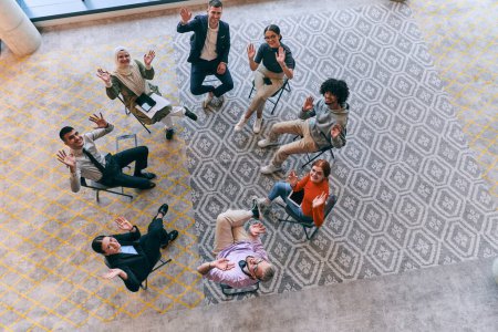 Foto de Vista superior de un grupo diverso de jóvenes emprendedores de negocios reunidos en un círculo para una reunión, discutiendo los desafíos corporativos y soluciones innovadoras dentro de los confines modernos de un gran - Imagen libre de derechos
