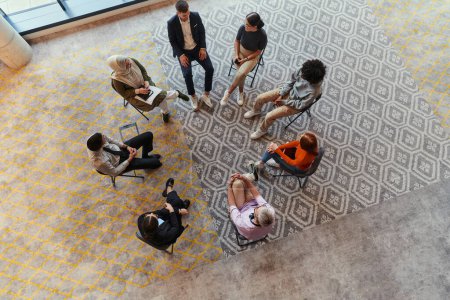 Foto de Vista superior de un grupo diverso de jóvenes emprendedores de negocios reunidos en un círculo para una reunión, discutiendo los desafíos corporativos y soluciones innovadoras dentro de los confines modernos de un gran - Imagen libre de derechos