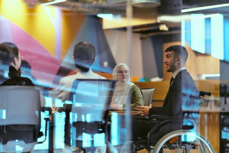 Foto de En una moderna oficina de startups de vidrio, un director en silla de ruedas lidera una reunión exitosa con sus colegas, incorporando la inclusividad y el trabajo en equipo. - Imagen libre de derechos