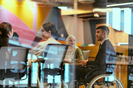 Téléchargez les photos : Dans un bureau moderne de démarrage du verre, un directeur en fauteuil roulant dirige une réunion réussie avec ses collègues, incarnant l'inclusivité et le travail d'équipe. - en image libre de droit