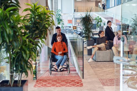 Photo for A company director assists his business colleague in a wheelchair, helping her navigate to their startup office, where they work alongside their diverse team of colleagues, emphasizing inclusivity and - Royalty Free Image