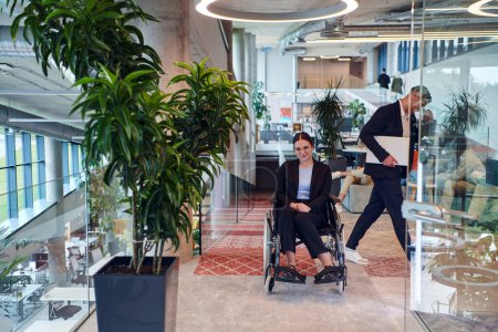Foto de En una oficina moderna, una joven mujer de negocios en silla de ruedas está rodeada por sus colegas de apoyo, encarnando el espíritu de inclusión y diversidad en el lugar de trabajo. - Imagen libre de derechos