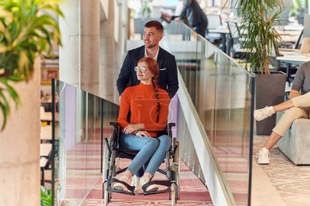 Photo for A company director assists his business colleague in a wheelchair, helping her navigate to their startup office, where they work alongside their diverse team of colleagues, emphasizing inclusivity and - Royalty Free Image