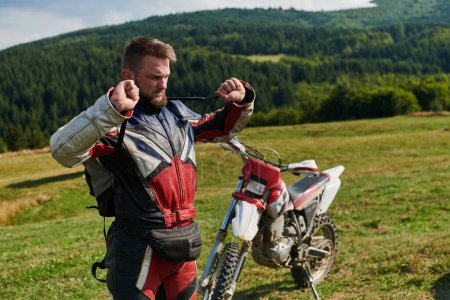 Téléchargez les photos : Un motocross professionnel, vêtu d'un costume complet, de gants et d'un sac à dos, se prépare pour une aventure audacieuse à travers la forêt, préparée pour un voyage hors route avec adrénaline. - en image libre de droit