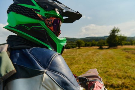 Téléchargez les photos : Un motocross professionnel, entièrement équipé avec casque, gants et lunettes, assis sur sa moto, prêt à se lancer dans une séance d'entraînement passionnante à travers la forêt difficile - en image libre de droit