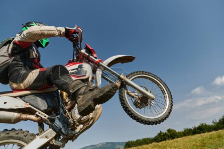 Photo for A fearless professional motocross rider skillfully executes an extreme back wheelie maneuver through a perilous forest terrain, showcasing remarkable balance and daring expertise. - Royalty Free Image