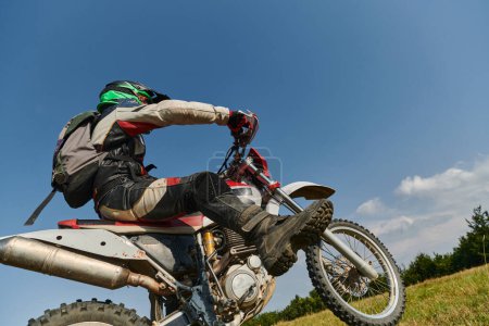Téléchargez les photos : Un motocross professionnel intrépide exécute habilement une manœuvre de roue arrière extrême à travers un terrain forestier périlleux, mettant en valeur un équilibre remarquable et une expertise audacieuse. - en image libre de droit