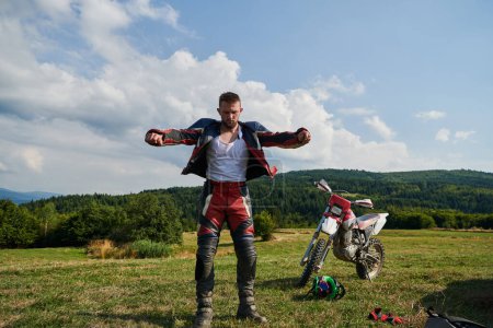 Téléchargez les photos : Un motocross professionnel, vêtu d'un costume complet, de gants et d'un sac à dos, se prépare pour une aventure audacieuse à travers la forêt, préparée pour un voyage hors route avec adrénaline. - en image libre de droit
