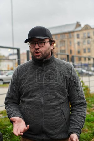 Photo for A man wearing a cap engages in a lively conversation with friends in the park, using animated hand gestures to convey his thoughts and adding to the casual and friendly atmosphere of their outdoor - Royalty Free Image
