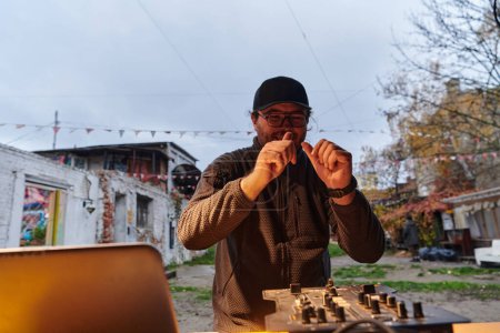 Foto de Un joven está entreteniendo a un grupo de amigos en el patio trasero de su casa, convirtiéndose en su DJ y tocando música en una reunión casual al aire libre. - Imagen libre de derechos