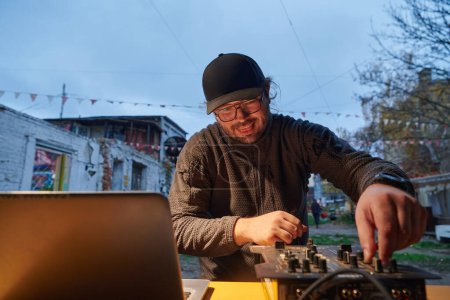 Téléchargez les photos : Un jeune homme divertit un groupe d'amis dans l'arrière-cour de sa maison, devenant leur DJ et jouant de la musique dans un rassemblement extérieur décontracté. - en image libre de droit