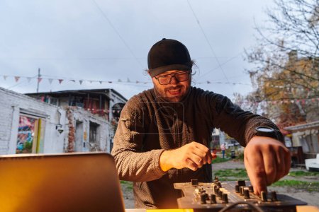 Photo for A young man is entertaining a group of friends in the backyard of his house, becoming their DJ and playing music in a casual outdoor gathering. - Royalty Free Image