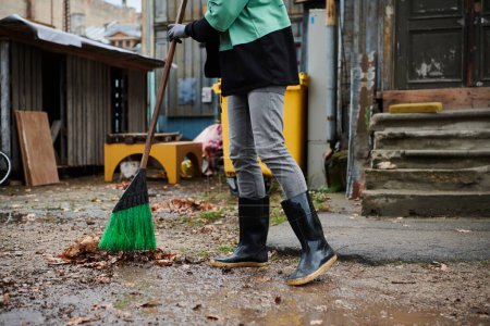 Téléchargez les photos : Une femme entretient le jardin avec diligence en ramassant de vieilles feuilles sèches, créant une scène pittoresque de soins en plein air et de propreté saisonnière. - en image libre de droit
