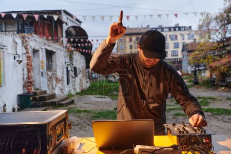 Téléchargez les photos : Un jeune homme divertit un groupe d'amis dans l'arrière-cour de sa maison, devenant leur DJ et jouant de la musique dans un rassemblement extérieur décontracté. - en image libre de droit