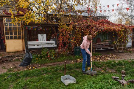 Téléchargez les photos : Un homme entretient le jardin avec diligence en ramassant de vieilles feuilles sèches, créant une scène pittoresque de soins en plein air et de propreté saisonnière - en image libre de droit