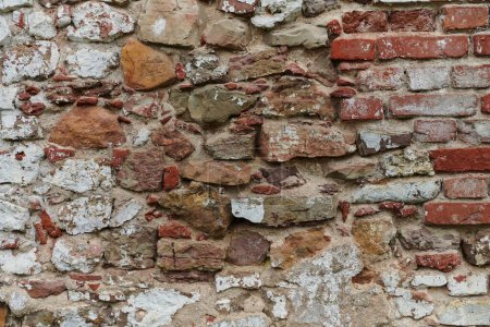 Foto de Una pared de ladrillo de piedra envejecida y envejecida, que muestra signos de decadencia e historia, se erige como un testimonio del tiempo y el desgaste.. - Imagen libre de derechos