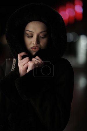 Photo for Muslim woman walking on an urban city street on a cold winter night wearing hijab with bokeh city lights in the background - Royalty Free Image