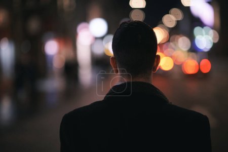 Téléchargez les photos : Souriant Meedle Eastern homme marchant dans la rue près de l'immeuble de bureaux moderne, homme d'affaires indépendant regardant loin tenant téléphone mobile sur la rue animée de la ville la nuit - en image libre de droit