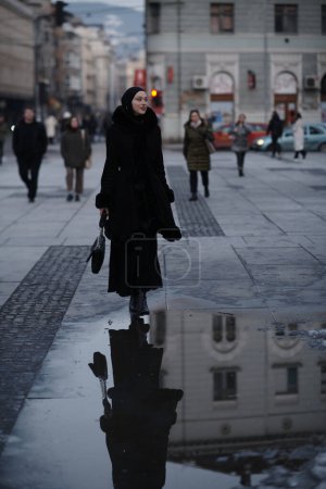 Foto de Mujer musulmana caminando en una calle urbana en una fría noche de invierno usando hijab con luces bokeh de la ciudad en el fondo - Imagen libre de derechos
