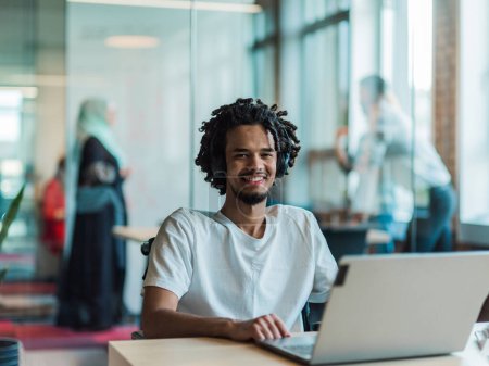 Photo for An African-American male, utilizing adaptive technology in his wheelchair, seamlessly integrates into a modern office space, embodying inclusivity and independence as he engages with a laptop - Royalty Free Image