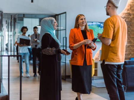 Photo for A group of young business colleagues, including a woman in a hijab, stands united in the modern corridor of a spacious startup coworking center, representing diversity and collaborative spirit. - Royalty Free Image