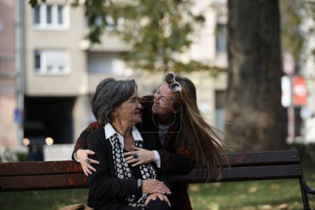 Foto de Anciana vieja linda mujer con Alzheimers muy feliz y sonriente cuando la hija mayor abraza y cuida de ella en el parque en otoño. Envejecimiento y crianza de los hijos, relaciones familiares y atención social. - Imagen libre de derechos