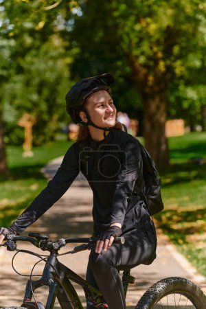 Foto de En el radiante abrazo de un día soleado, una mujer moderna disfruta de la alegría del ciclismo, su elegante bicicleta y su equipo profesional complementando su estilo de vida activo mientras pasea por el parque - Imagen libre de derechos