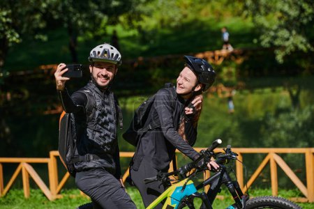 Foto de Una pareja moderna captura la alegría de su paseo en bicicleta en el parque a través de un selfie de moda, mezcla de tecnología y aventura al aire libre para inmortalizar un momento de felicidad y unidad. - Imagen libre de derechos