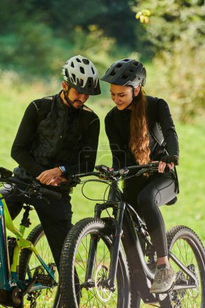 Foto de Una dulce pareja, equipada con bicicletas y absorta en la coordinación de su viaje, comprueba su móvil GPS y observa mientras planifica rutas escénicas en el parque, mezclando a la perfección la tecnología y - Imagen libre de derechos