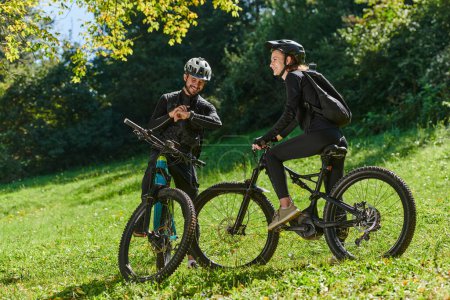 Téléchargez les photos : Un couple doux, équipé de vélos et absorbé dans la coordination de leur voyage, vérifie leur GPS mobile et les montres tout en planifiant des itinéraires pittoresques dans le parc, mélangeant parfaitement la technologie et - en image libre de droit