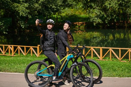 Foto de Una pareja moderna captura la alegría de su paseo en bicicleta en el parque a través de un selfie de moda, mezcla de tecnología y aventura al aire libre para inmortalizar un momento de felicidad y unidad. - Imagen libre de derechos