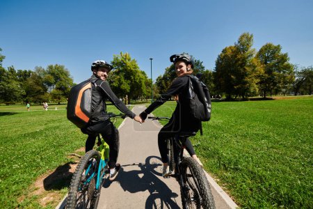 Photo for A sweet couple, adorned in cycling gear, rides their bicycles, their hands interlocked in a romantic embrace, capturing the essence of love, adventure, and joy on a sunlit path. - Royalty Free Image