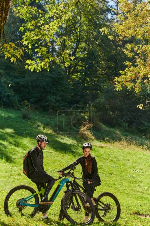 Foto de Una dulce pareja, equipada con bicicletas y absorta en la coordinación de su viaje, comprueba su móvil GPS y observa mientras planifica rutas escénicas en el parque, mezclando a la perfección la tecnología y - Imagen libre de derechos