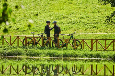 Foto de Una pareja feliz, adornada con equipo de ciclismo profesional, disfruta de un romántico paseo en bicicleta a través de un parque, rodeado de modernas atracciones naturales, irradiando amor y felicidad. - Imagen libre de derechos