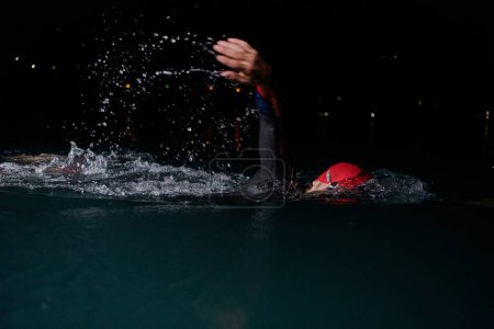 Photo for A determined professional triathlete undergoes rigorous night time training in cold waters, showcasing dedication and resilience in preparation for an upcoming triathlon swim competition. - Royalty Free Image