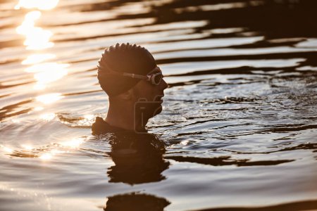 Téléchargez les photos : Un triathlète trouve un rajeunissement serein dans un lac, se prélassant dans la tranquillité de l'eau après une séance d'entraînement intense. - en image libre de droit