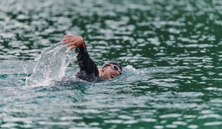 Téléchargez les photos : Un triathlète professionnel s'entraîne avec un dévouement inébranlable pour une compétition à venir au bord d'un lac, émettant un sentiment d'athlétisme et un profond engagement envers l'excellence - en image libre de droit