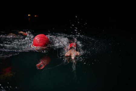 Téléchargez les photos : Un triathlète professionnel déterminé subit un entraînement nocturne rigoureux dans les eaux froides, faisant preuve de dévouement et de résilience en préparation d'une prochaine compétition de natation de triathlon. - en image libre de droit