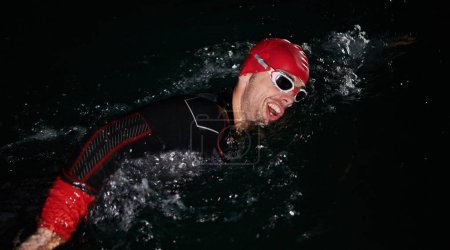 Foto de Un determinado triatleta profesional se somete a un riguroso entrenamiento nocturno en aguas frías, mostrando dedicación y resiliencia en preparación para una próxima competición de natación de triatlón.. - Imagen libre de derechos